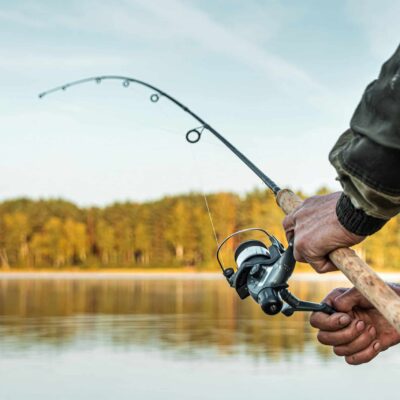 Hands of a man in a Urp plan hold a fishing rod, a fisherman catches fish at dawn. Fishing hobby vacation concept. Copy space